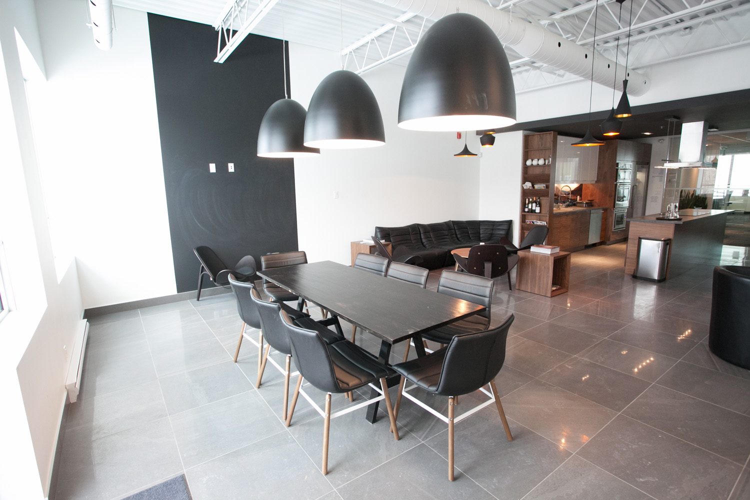 L’aire de rencontre des bureaux : table noire, chaises de cuir, suspensions noires, cuisine témoin au fond